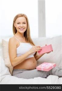 pregnancy, motherhood and celebration concept - smiling pregnant woman sitting on sofa with opened gift box