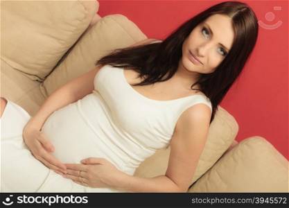 Pregnancy, motherhood and happiness concept. Beautiful stylish elegant pregnant woman in white short dress relaxing on sofa touching her belly, at home