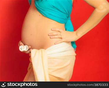 Pregnancy, motherhood and happiness concept. Closeup pregnant woman holding dummy for the unborn baby on red background