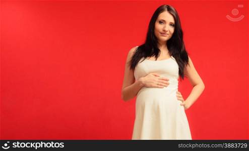 Pregnancy, motherhood and happiness concept. Elegant pregnant woman in white dress touching her belly