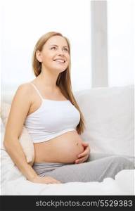 pregnancy, motherhood and happiness concept - happy pregnant woman sitting on sofa and touching her belly and dreaming