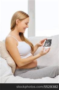 pregnancy, motherhood and happiness concept - happy pregnant woman sitting on sofa with ultrasound picture