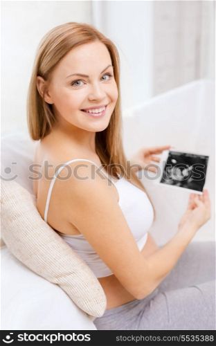pregnancy, motherhood and happiness concept - happy pregnant woman sitting on sofa with ultrasound picture