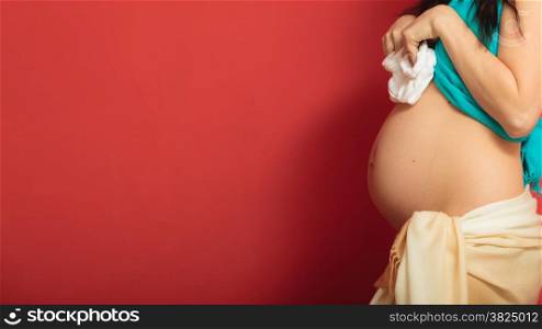 Pregnancy, motherhood and happiness concept. pregnant woman holding small shoes boots for the unborn baby on red background