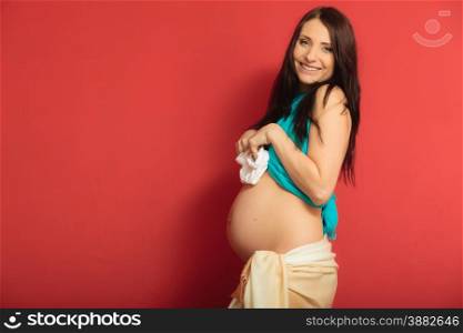 Pregnancy, motherhood and happiness concept. pregnant woman holding small shoes boots for the unborn baby on red background