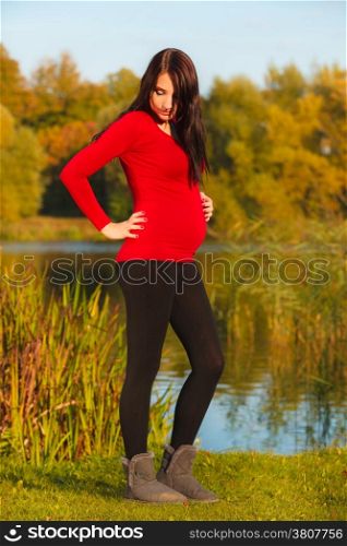 Pregnancy, motherhood and happiness concept. Relaxed calm pregnant woman walking outside in autumn park
