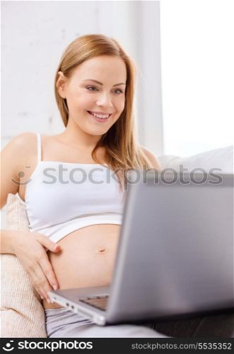 pregnancy, motherhood and technology concept - smiling pregnant woman sitting on sofa with laptop computer