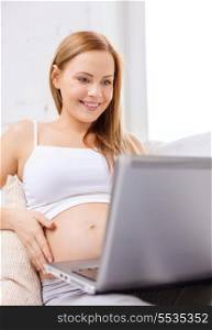 pregnancy, motherhood and technology concept - smiling pregnant woman sitting on sofa with laptop computer