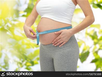 pregnancy, motherhood, control, people and expectation concept - close up of happy pregnant woman measuring her bare tummy over green tree leavers background