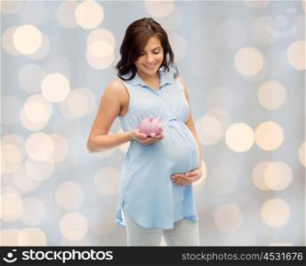 pregnancy, motherhood, finance, saving and people concept - happy pregnant woman with piggybank over holidays lights background