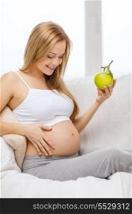 pregnancy, motherhood, healthcare, food and happiness concept - happy pregnant woman sitting on sofa with fresh green apple