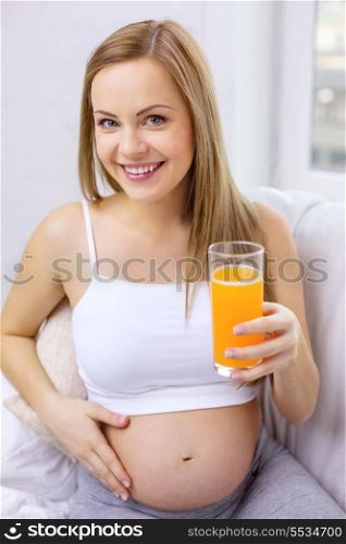 pregnancy, motherhood, healthcare, food and happiness concept - happy pregnant woman sitting on sofa with fresh orange juice