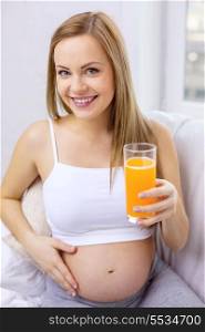pregnancy, motherhood, healthcare, food and happiness concept - happy pregnant woman sitting on sofa with fresh orange juice