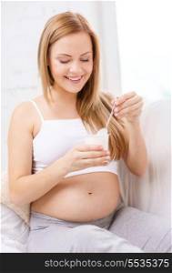 pregnancy, motherhood, healthcare, food and happiness concept - happy pregnant woman sitting on sofa with yogurt and spoon
