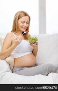 pregnancy, motherhood, healthcare, food and happiness concept - happy pregnant woman sitting on sofa eating salad