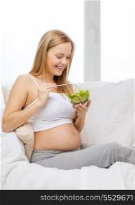 pregnancy, motherhood, healthcare, food and happiness concept - happy pregnant woman sitting on sofa eating salad