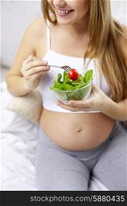 pregnancy, motherhood, healthcare, food and people concept - close up of happy pregnant woman sitting on sofa with bowl of salad