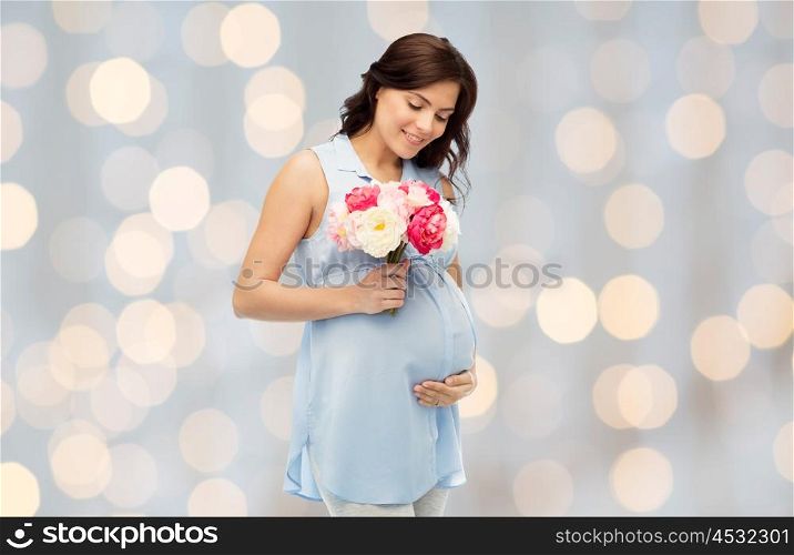 pregnancy, motherhood, holidays, people and expectation concept - happy pregnant woman with flowers touching her big belly over holidays lights background