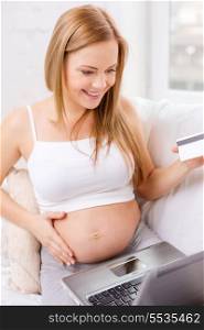 pregnancy, motherhood, money, internet and technology concept - smiling pregnant woman sitting on sofa with laptop computer and credit card