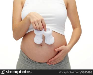 pregnancy, motherhood, people and expectation concept - close up of happy pregnant woman touching her bare tummy and holding babys bootees
