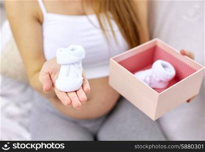 pregnancy, motherhood, people and expectation concept - close up of happy pregnant woman holding box with babys bootees at home