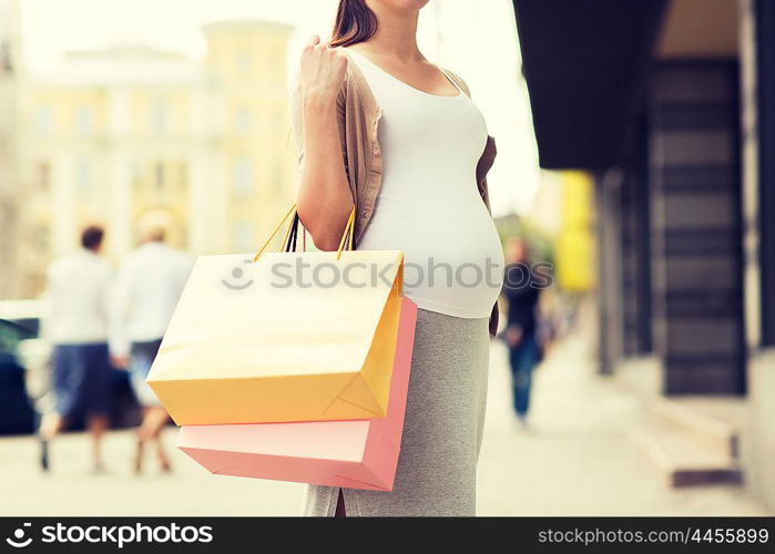 pregnancy, motherhood, people and expectation concept - close up of pregnant woman with shopping bags at city street