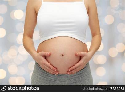 pregnancy, motherhood, people and expectation concept - close up of pregnant woman touching her bare tummy over holiday lights background
