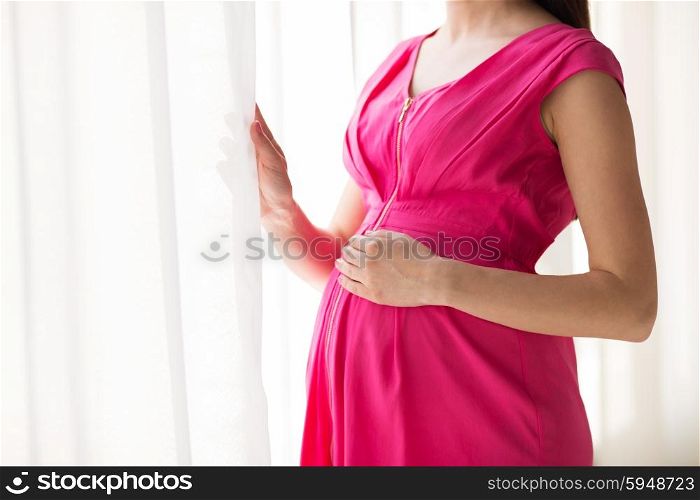 pregnancy, motherhood, people and expectation concept - close up of pregnant woman looking through window at home