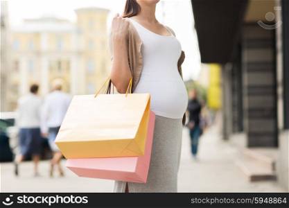 pregnancy, motherhood, people and expectation concept - close up of pregnant woman with shopping bags at city street