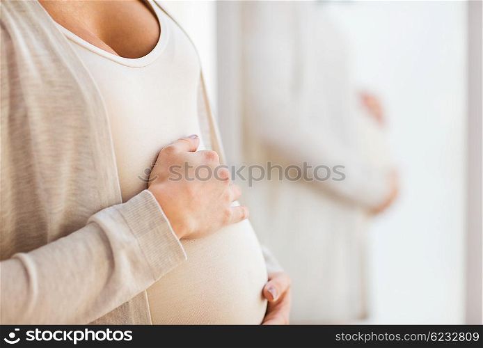pregnancy, motherhood, people and expectation concept - close up of pregnant woman belly at mirror