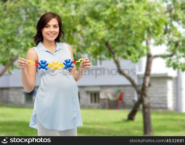 pregnancy, motherhood, people and expectation concept - happy pregnant woman holding rattle toy over summer garden and house background