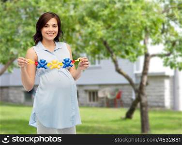 pregnancy, motherhood, people and expectation concept - happy pregnant woman holding rattle toy over summer garden and house background