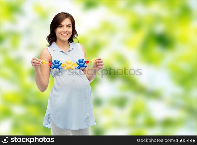 pregnancy, motherhood, people and expectation concept - happy pregnant woman holding rattle toy over green natural background