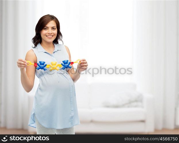 pregnancy, motherhood, people and expectation concept - happy pregnant woman holding rattle toy over home living room background