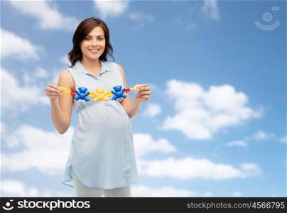 pregnancy, motherhood, people and expectation concept - happy pregnant woman holding rattle toy over blue sky and clouds background