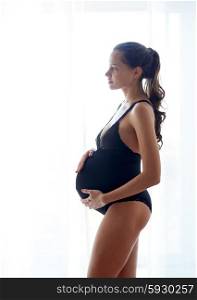 pregnancy, motherhood, people and expectation concept - happy pregnant woman in black underwear near window at home
