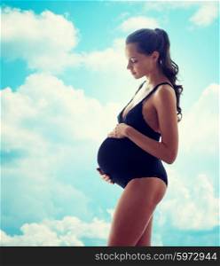 pregnancy, motherhood, people and expectation concept - happy pregnant woman in black underwear over blue sky and clouds background