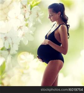 pregnancy, motherhood, people and expectation concept - happy pregnant woman in black underwear over green background with flowers