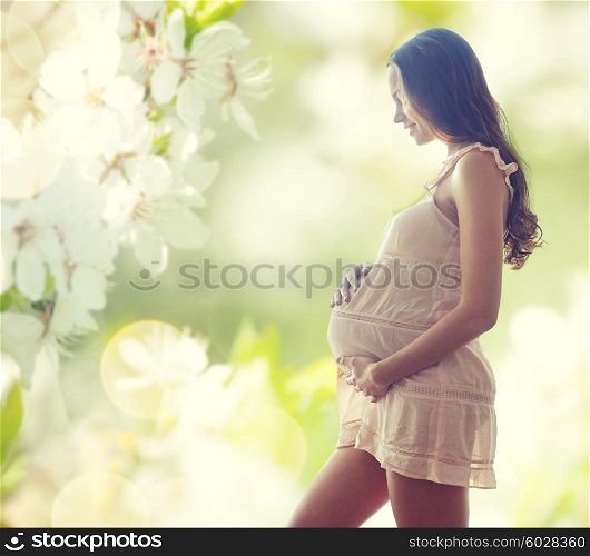 pregnancy, motherhood, people and expectation concept - happy pregnant woman in chemise over green background with flowers