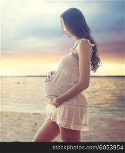 pregnancy, motherhood, people and expectation concept - happy pregnant woman in chemise over sunset on beach background