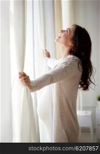 pregnancy, motherhood, people and expectation concept - happy pregnant woman opening window curtains at home