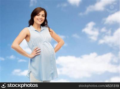 pregnancy, motherhood, people and expectation concept - happy pregnant woman touching her big belly over blue sky and clouds background