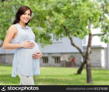 pregnancy, motherhood, people and expectation concept - happy pregnant woman touching her big belly over summer garden and house background
