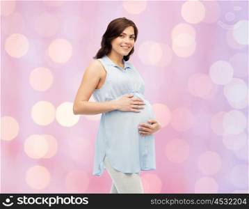 pregnancy, motherhood, people and expectation concept - happy pregnant woman touching her big belly over rose quartz and serenity holidays lights background