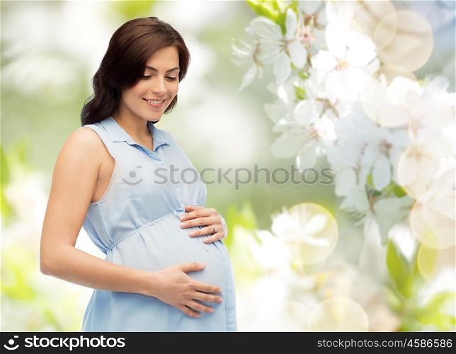 pregnancy, motherhood, people and expectation concept - happy pregnant woman touching her big belly over natural spring cherry blossom background
