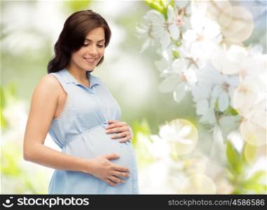 pregnancy, motherhood, people and expectation concept - happy pregnant woman touching her big belly over natural spring cherry blossom background