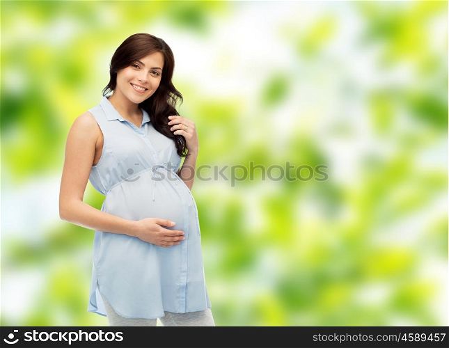 pregnancy, motherhood, people and expectation concept - happy pregnant woman touching her big belly over green natural background