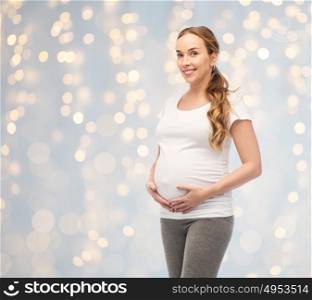 pregnancy, motherhood, people and expectation concept - happy pregnant woman touching her big belly over holidays lights background. happy pregnant woman touching her big belly
