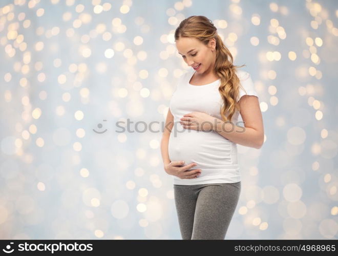 pregnancy, motherhood, people and expectation concept - happy pregnant woman touching her big belly over holidays lights background. happy pregnant woman touching her big belly