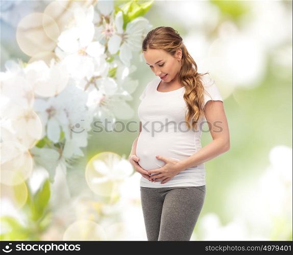 pregnancy, motherhood, people and expectation concept - happy pregnant woman touching her big belly over natural spring cherry blossom background. happy pregnant woman touching her big belly